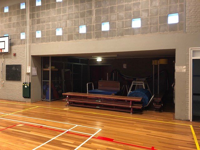 foto van gymzaal betonnen wand en opslagruimte vol met gymtoestellen zoals een bank