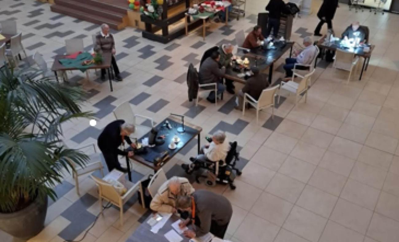 tafels met vrijwillers die ieder een bezoeker helpen met het repareren van een kapot apparaat