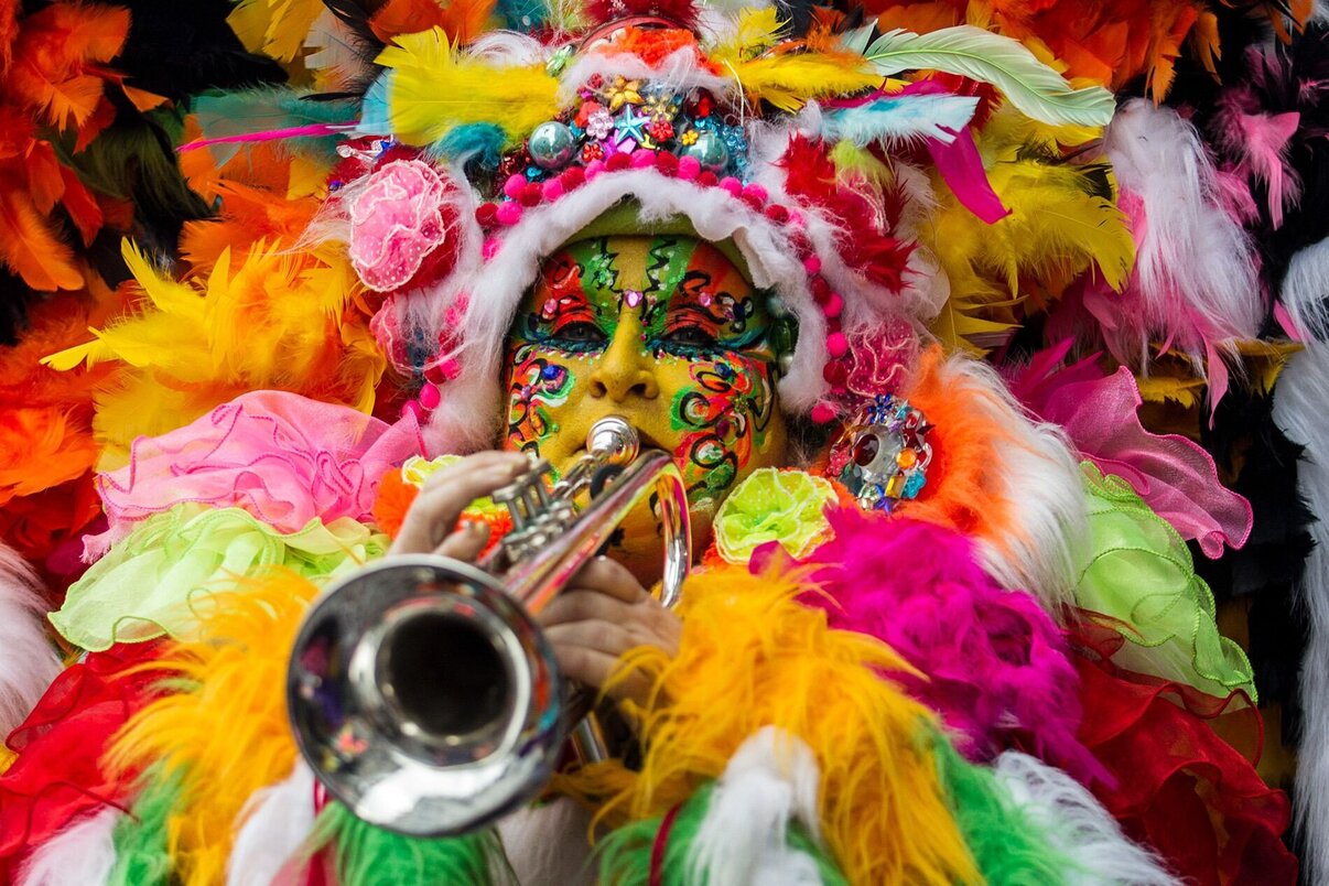 een vrouw verkleed met een gekleurd verenpak en een trompet in haar handen