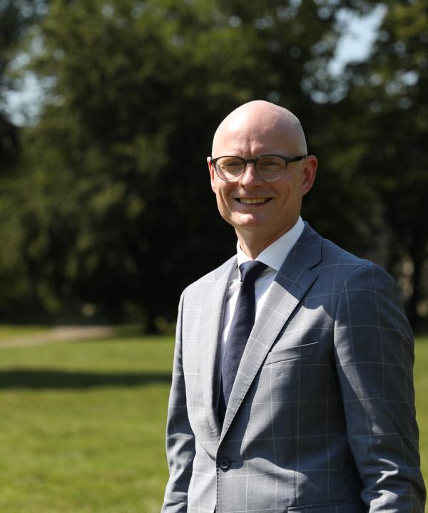 Foto van wethouder Hubert Mackus, een witte man met een bril, in een donkergrijs pak met stropdas