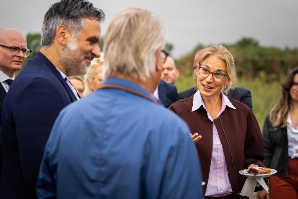 Vrouw in bordeauxrode jas praat met bezoekers tijdens een werkbezoek aan de Spoorzone Maastricht.