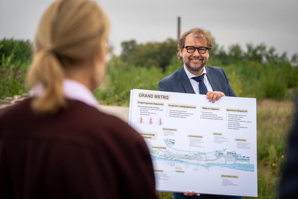 Man toont een informatiebord over de ontwikkeling van de Spoorzone Maastricht aan een groep bezoekers.