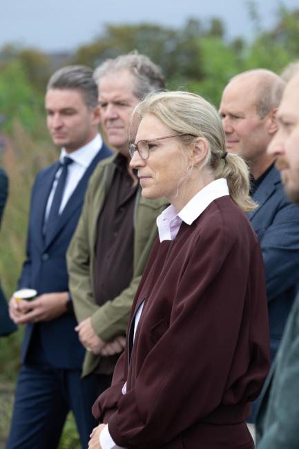 Vrouw in bordeauxrode jas luistert aandachtig tijdens een werkbezoek aan de Spoorzone Maastricht.